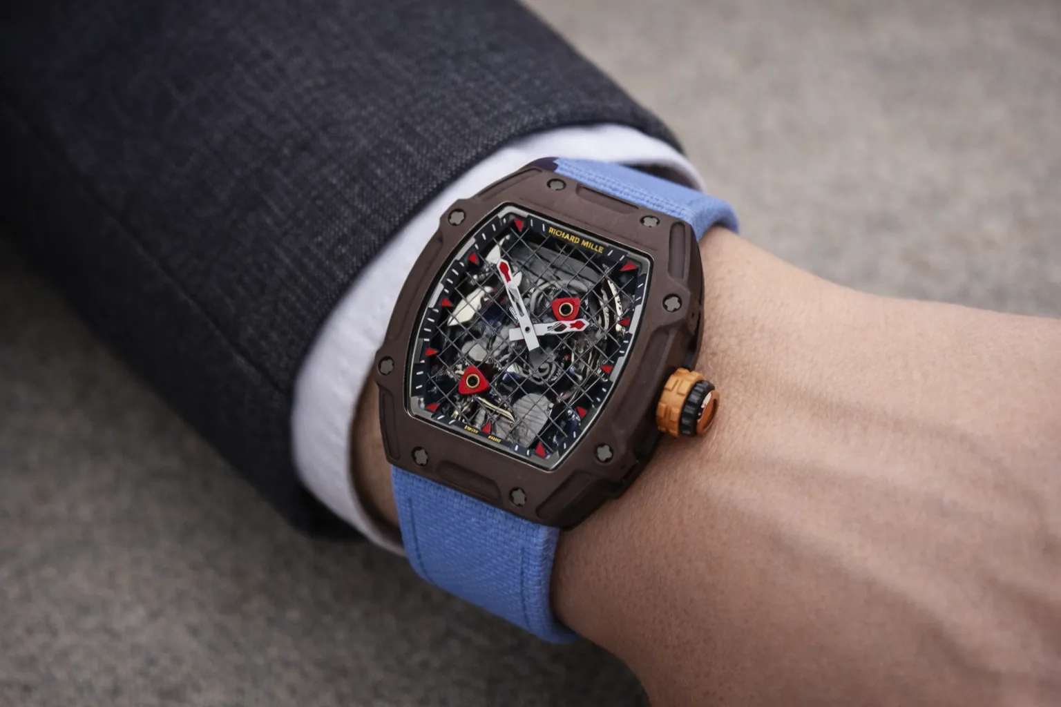 Premium on-wrist shot of the Richard Mille RM 27-04 replica, the iconic Rafael Nadal tennis-inspired timepiece. Featuring a lightweight brown carbon TPT tonneau case, a skeletonized dial with red tennis racket accents, and a sporty blue fabric strap. This super clone delivers the legendary RM ultra-light design and high-performance horology for collectors.