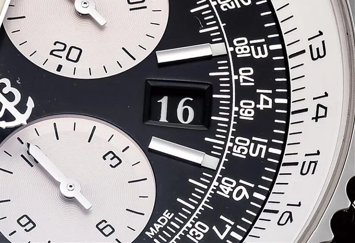Makroaufnahme des Zifferblatts des Bell & Ross Navitimer Chronographen, das strukturierte Unterzifferblätter, klare gedruckte Tachymeter-Markierungen, Ankeremblem und Datumsanzeigefenster zeigt. Vollständiger Bedienungsleitfaden für die verschraubte Krone des Modells: zuerst lösen, bevor Datum/Zeit angepasst wird, Datumseinstellung zwischen 21 Uhr und 3 Uhr vermeiden, um Getriebeschäden zu verhindern, Krone nach der Einstellung vollständig verriegeln, um die wasserdichte Abdichtung zu erhalten.