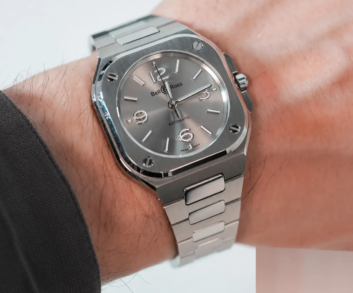 Wrist lifestyle shot of polished Bell & Ross BR05 silver dial replica with integrated metal bracelet. The lug design directly determines wearing experience for bony-wrist wearers. Vintage BR 03’s split straight lugs lack flexibility, sitting fully on wrist bone bumps and triggering friction & tilting. BR05’s one-piece curved integrated lugs naturally follow wrist curves, distributing weight on soft tissue rather than bony protrusions to stop pinching and sliding. If you prefer BR03, pick tapered lug styles and stay away from stiff extended lugs that amplify pressure discomfort.